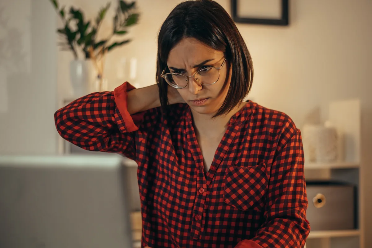 Mal di testa e cervicale legati alla vista, esame visuo posturale Ottica Contin: donna con occhiali si massaggia il collo davanti al computer